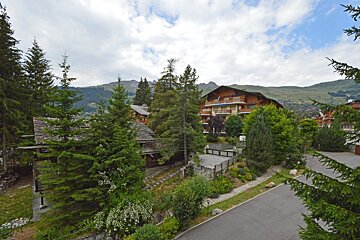 A large building in the middle of a forest with mountains in the background