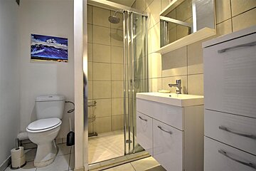 A compact, modern bathroom features a toilet, glass shower, white sink vanity with mirror, and storage cabinets, with a mountain artwork on the wall.