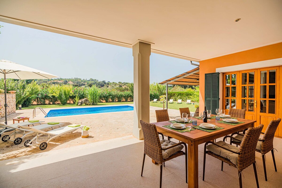A table and chairs on a patio with a pool in the background
