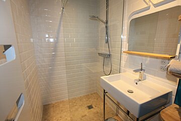 A modern bathroom featuring a walk-in shower with white subway tiles, a glass partition, and a sleek sink with a mirror above it.