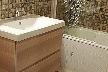 Modern bathroom featuring a white sink on a light wood vanity next to a bathtub with a patterned glass screen and mosaic tiled walls.