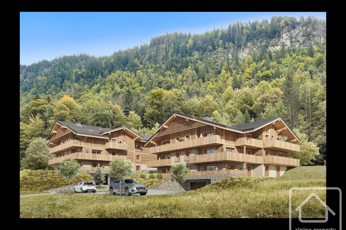 Two modern wooden chalet-style buildings with balconies are nestled into a lush, forested mountainside under a clear blue sky.