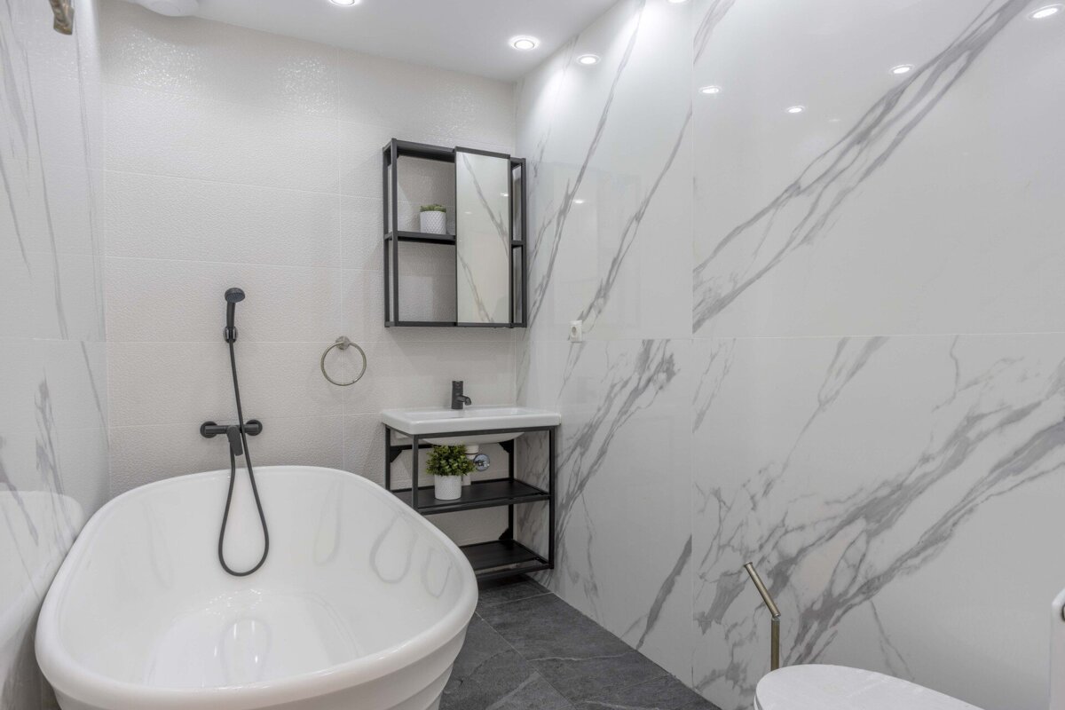 A sleek, modern white bathroom features a freestanding tub, black fixtures, a minimalist vanity, and stylish white-and-grey marble-patterned walls.