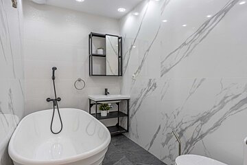 A sleek, modern white bathroom features a freestanding tub, black fixtures, a minimalist vanity, and stylish white-and-grey marble-patterned walls.
