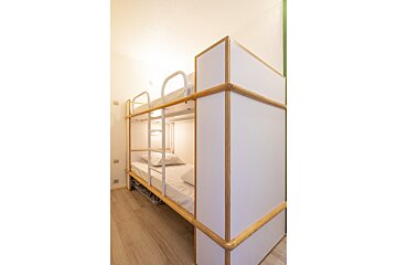 Clean, modern bunk beds with white mattresses, wooden frames, and individual lights in a bright room with light wood flooring.