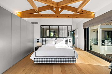 Modern bedroom with exposed wooden beams, a checkered bed, built-in wardrobes, and sliding glass doors leading to a balcony.
