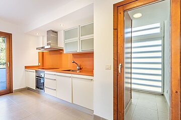 Modern kitchen with orange backsplash, white cabinets, stainless appliances, and a wooden door leading to a bright room with striped blinds.
