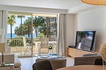 Bright, modern living room with a balcony offering views of palm trees and the ocean.