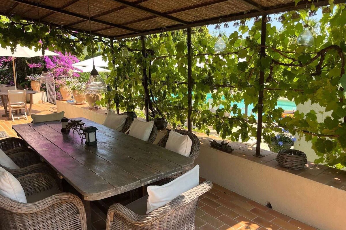 A table and chairs under a canopy with a pool in the background