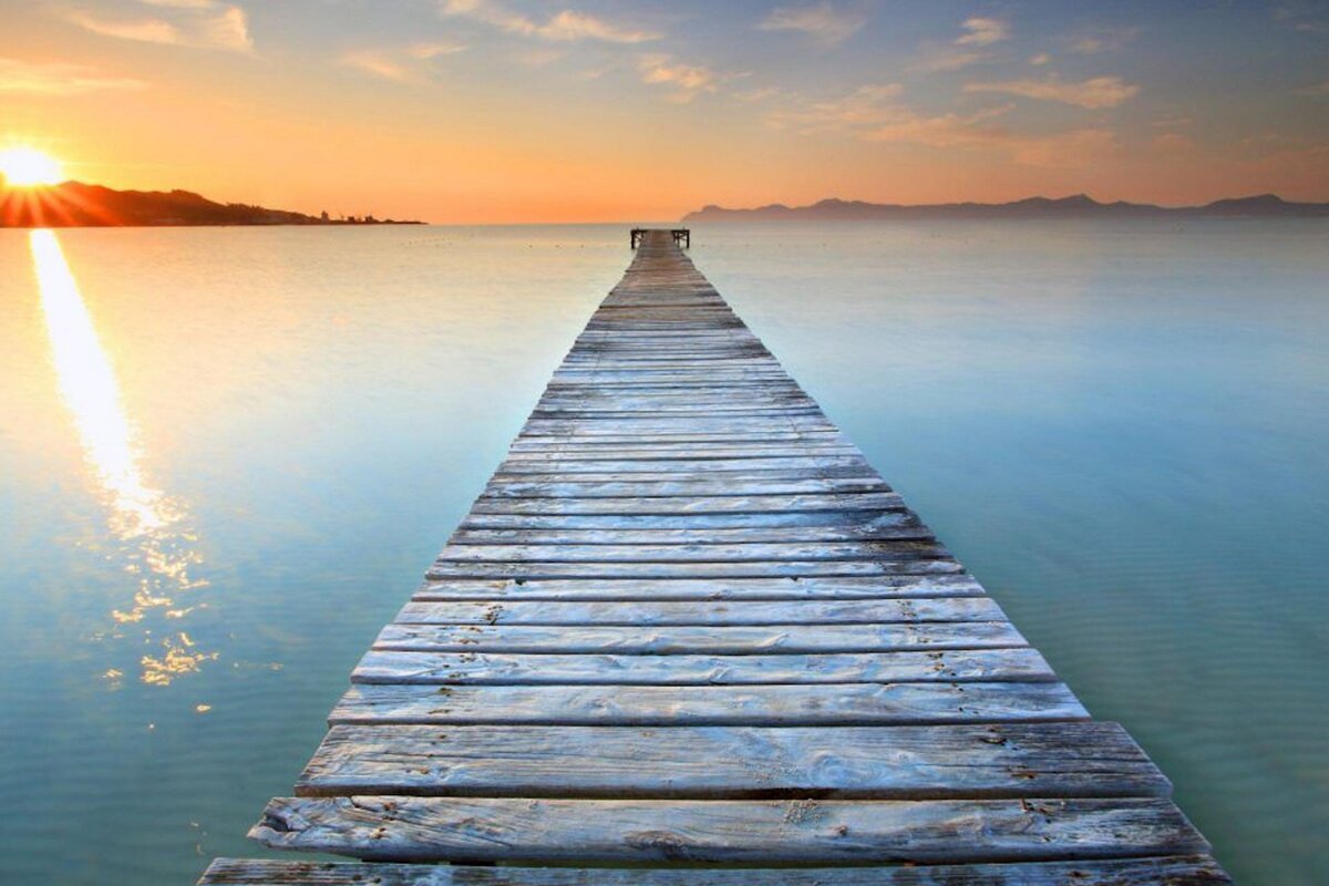 A wooden pier leading into the ocean at sunset