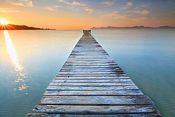 A wooden pier leading into the ocean at sunset