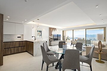 Stylish open-plan apartment with a modern kitchen, dining area, and living space opening to a balcony with a panoramic ocean view.