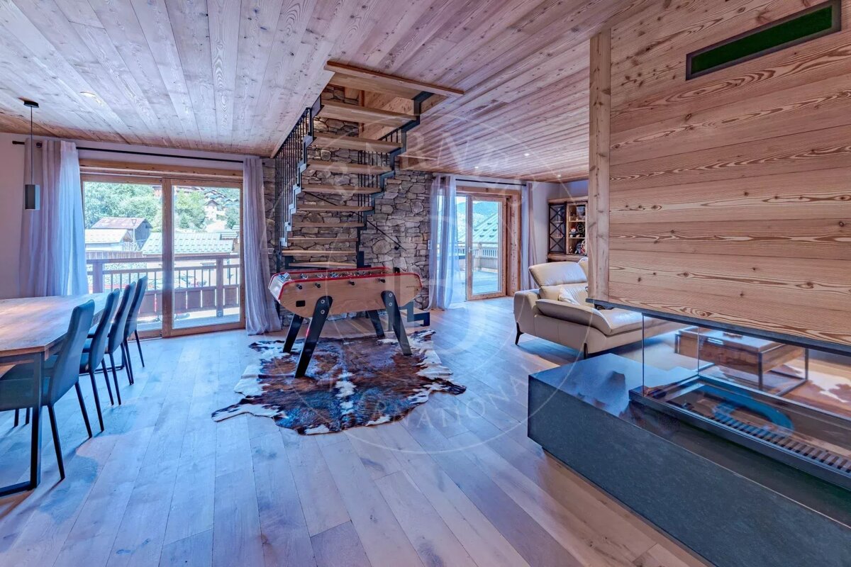 Rustic-modern chalet with wood and stone finishes. Features a spiral staircase, foosball table, dining area, and a sleek fireplace.