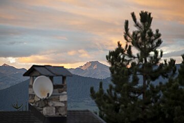 A chimney with a satellite dish on top of it with mountains in the background