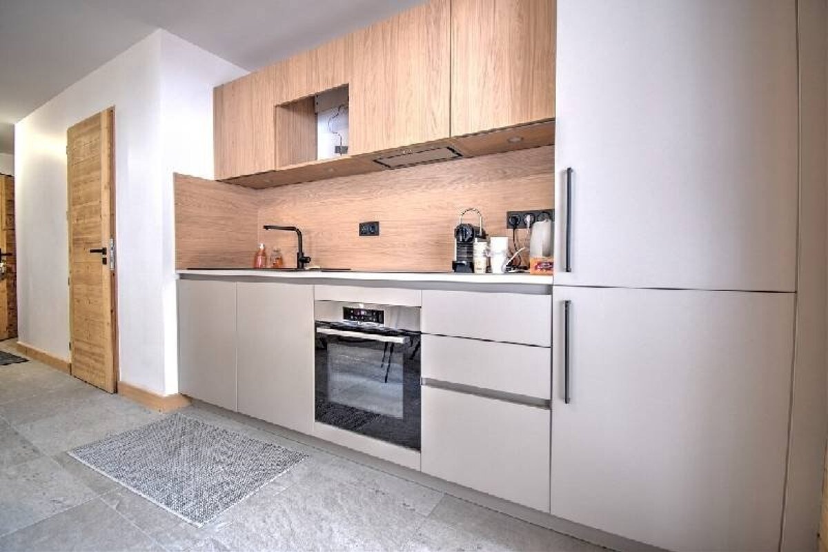 A modern, minimalist kitchen featuring light wood upper cabinets and backsplash, white lower cabinets, and integrated appliances.