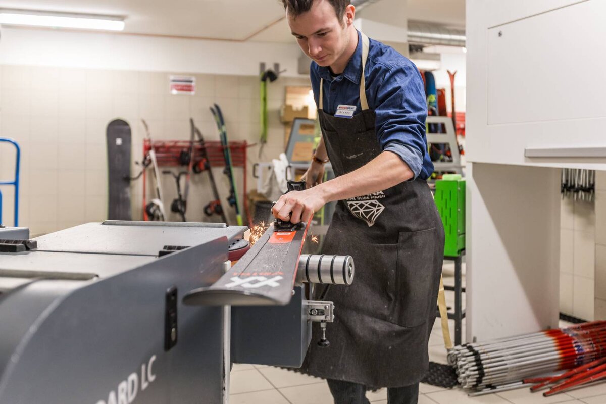 A man sharpens a ski with a machine that says lc