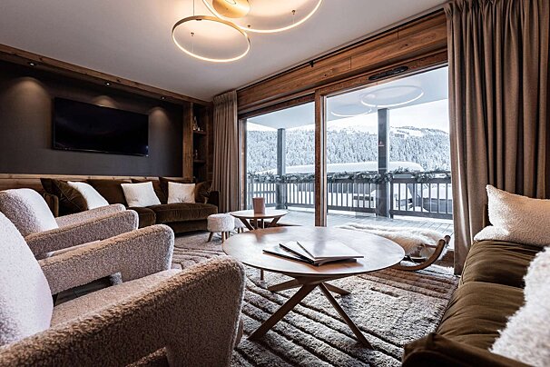 A luxurious, cozy living room with plush seating, warm lighting, and a stunning snowy mountain view through large glass doors.