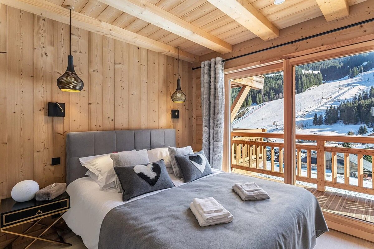 Cozy wooden bedroom with a bed and a balcony, offering stunning views of a snowy mountain ski slope and forest.