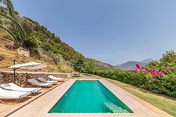 A swimming pool surrounded by chairs and umbrellas with mountains in the background