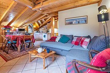 Cozy cabin living room with a sloped wooden ceiling, gray sectional sofa, and dining area in the background.