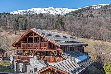 A large wooden house in the mountains with snow on the roof