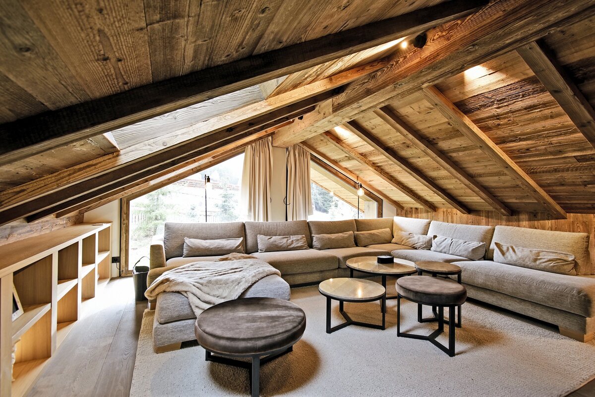 A cozy, modern chalet living room features a wooden vaulted ceiling, plush sectional sofa, stylish coffee tables, and large windows.