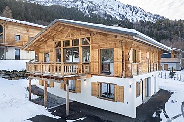 A beautiful wooden and white stucco alpine chalet nestled in a snowy mountain landscape.