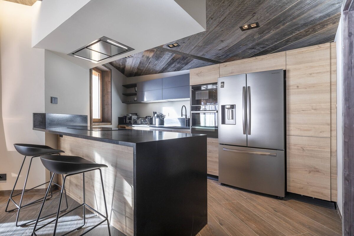 Modern kitchen with wood cabinets, a black island with two stools, a stainless steel refrigerator, and a dark wood ceiling.