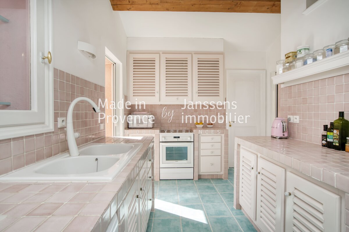 A kitchen with pink tiles and white cabinets made in provence by immobilier