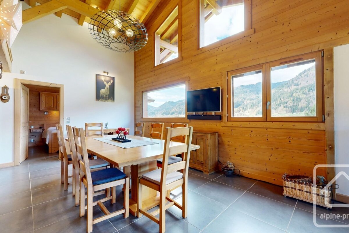 A warm, wood-paneled dining room with a long table, modern lighting, and large windows offering scenic mountain views.