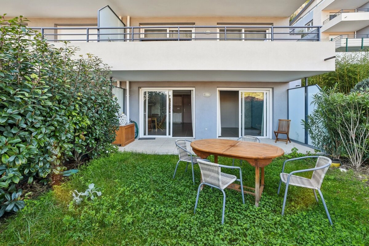 Ground-floor apartment with a private grassy yard featuring a wooden dining table, chairs, and sliding glass doors.