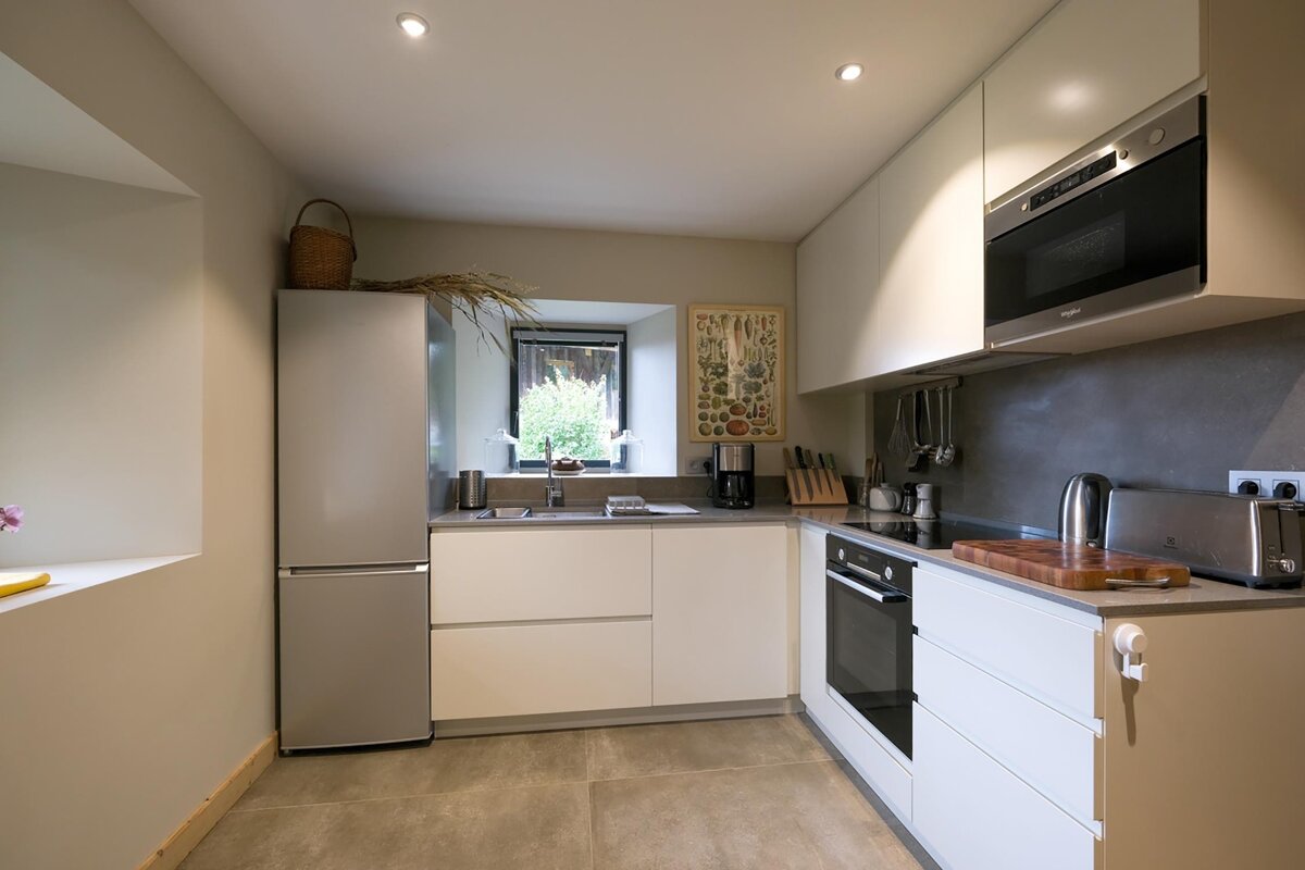 A modern, L-shaped kitchen featuring light cabinets, stainless steel appliances, a window over the sink, and neutral tones for a clean, contemporary feel.