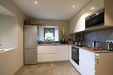 A modern, L-shaped kitchen featuring light cabinets, stainless steel appliances, a window over the sink, and neutral tones for a clean, contemporary feel.