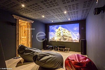 A cozy home theater room with beanbag chairs, a rustic wooden door, and a large projection screen displaying a movie logo.
