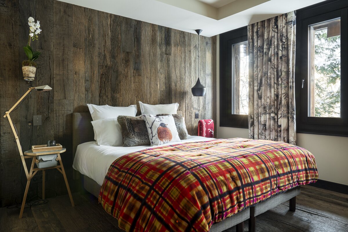 A bedroom with a wooden wall and a bed with a plaid blanket