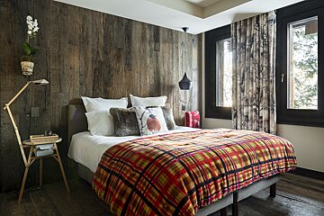 A bedroom with a wooden wall and a bed with a plaid blanket