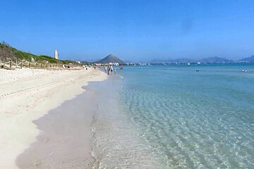 A beach with a mountain in the background and clear water