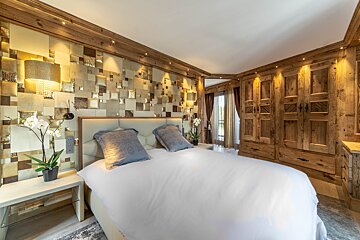 Luxurious modern rustic bedroom with a gold textured accent wall, wooden paneling, warm lighting, and a plush white bed.