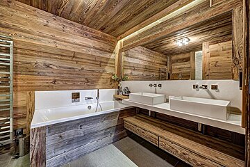 Modern rustic bathroom with wooden walls and ceiling, featuring a built-in bathtub and double white vessel sinks.