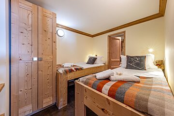 Cozy twin bedroom with light wooden beds, a large wardrobe, and warm blankets. A ski-themed pillow and teddy bear add charming details.