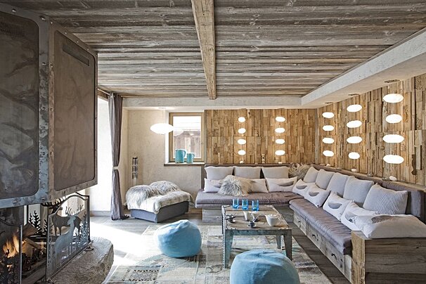 A cozy, rustic chalet living room with textured wooden walls and ceiling, a fireplace, comfortable seating, and unique illuminated wall panels.