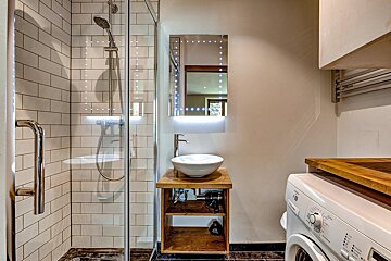 Modern bathroom featuring a tiled shower, bowl sink with lighted mirror, and a washing machine.