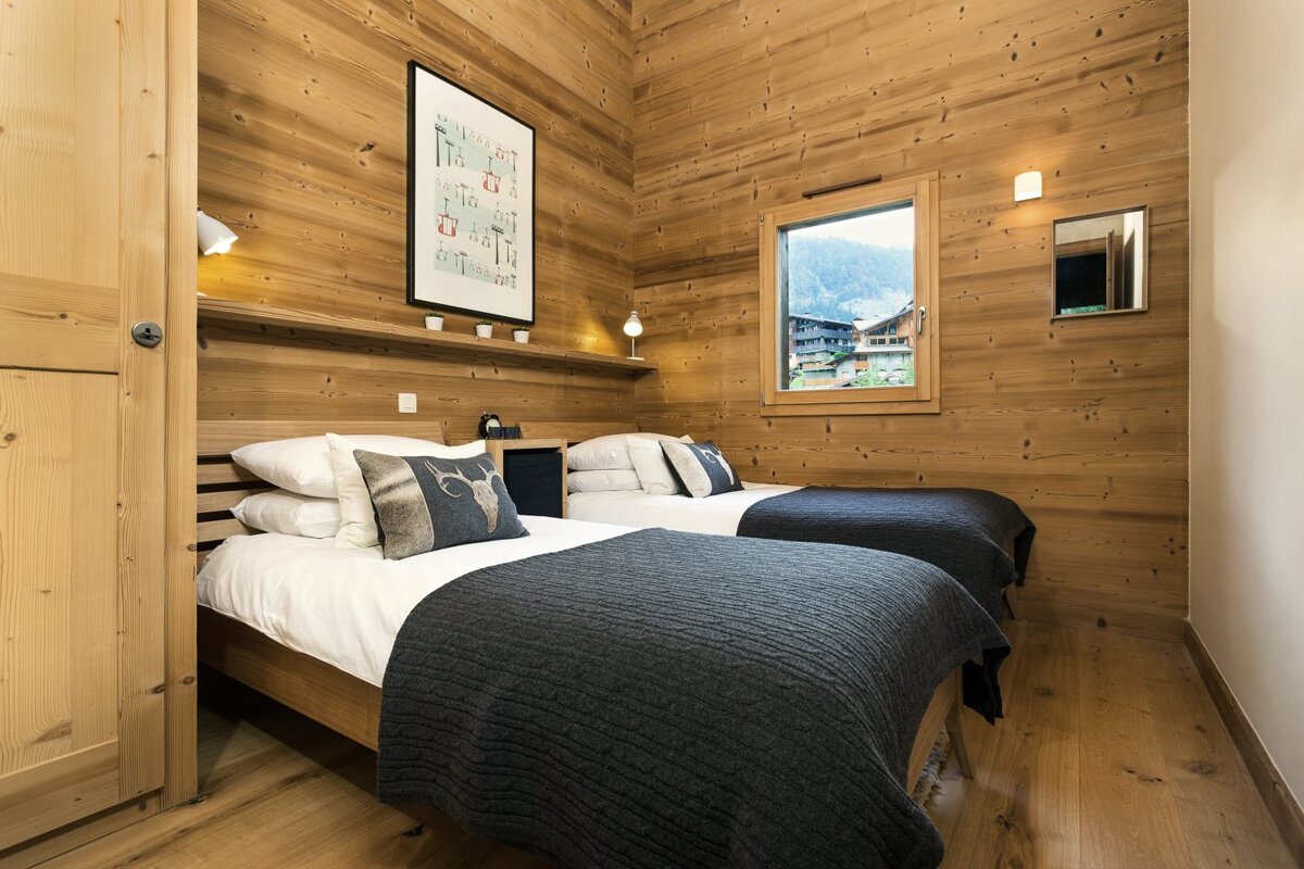 A cozy, wood-paneled twin bedroom with dark grey blankets, mountain views from the window, and cabin-style decor.
