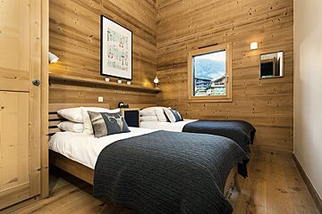 A cozy, wood-paneled twin bedroom with dark grey blankets, mountain views from the window, and cabin-style decor.