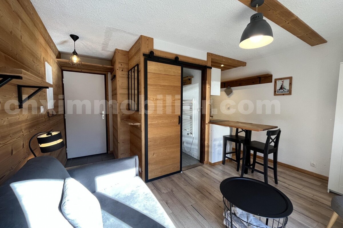 Cozy room with wood-paneled walls, grey sofa, bar dining, and a sliding barn door. Features industrial lighting and light wood floors.