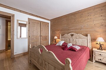 Rustic bedroom featuring a wooden bed with heart cutouts, red bedding, paneled walls, and matching furniture.