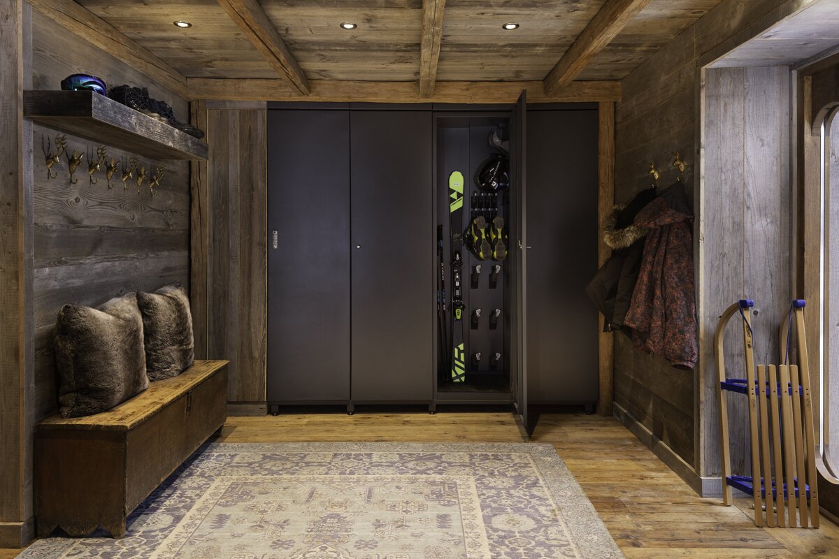 Rustic ski chalet mudroom with wooden walls/ceiling, a ski gear cabinet, storage bench, and sleds.