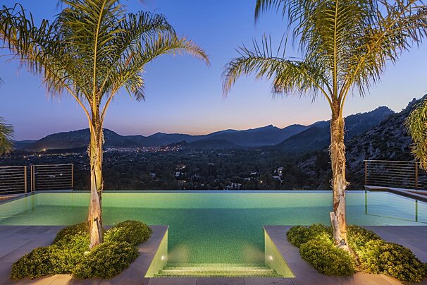 A swimming pool with palm trees and mountains in the background