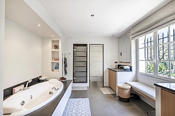 A modern, spacious bathroom with a large jacuzzi tub, tiled floors, frosted glass doors, and a large window.