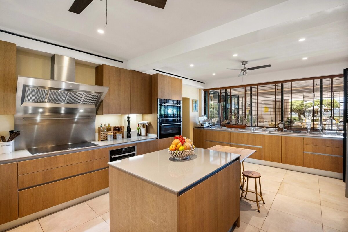 Modern kitchen with light wood cabinets, a large central island, stainless steel appliances, and bright tile flooring.